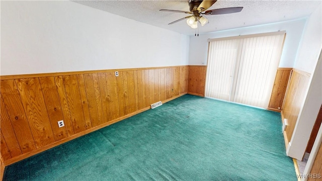 unfurnished bedroom with dark colored carpet, ceiling fan, a textured ceiling, and wood walls