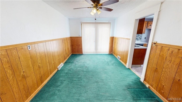 carpeted empty room with ceiling fan, a textured ceiling, and wood walls