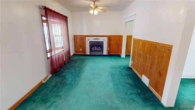 unfurnished living room with ceiling fan, wooden walls, and dark colored carpet