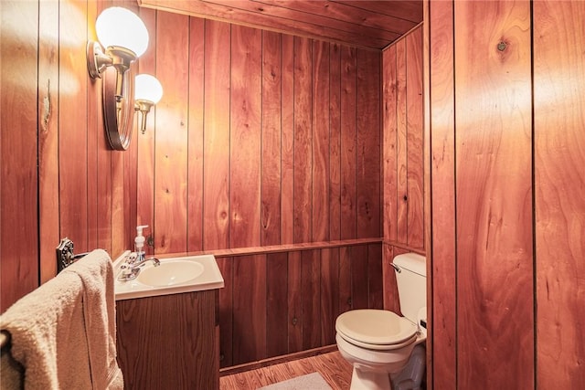 bathroom with vanity, toilet, and wood walls