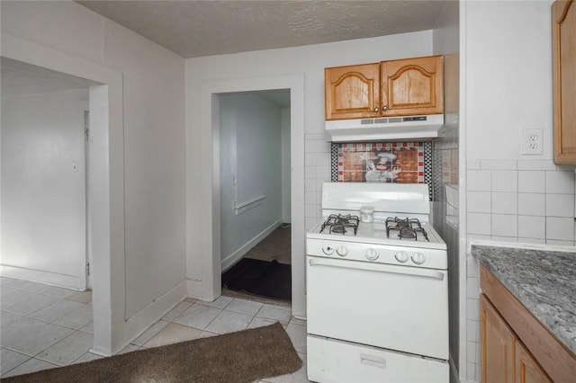 kitchen with tasteful backsplash, light tile patterned floors, white gas range oven, and a textured ceiling