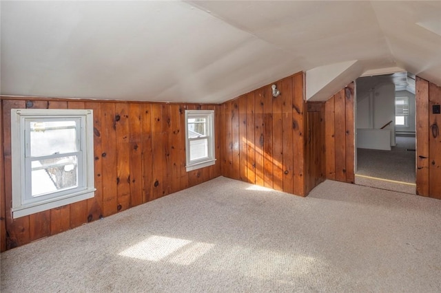 bonus room with vaulted ceiling, carpet flooring, and wood walls