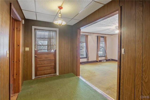 carpeted entryway with a paneled ceiling and wood walls