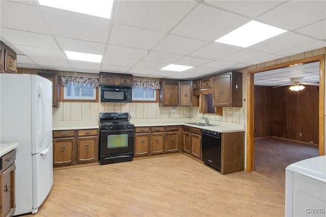 kitchen with wooden walls, washer / dryer, sink, black appliances, and light hardwood / wood-style flooring