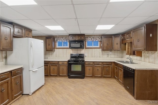 kitchen with sink, light hardwood / wood-style flooring, a drop ceiling, and black appliances