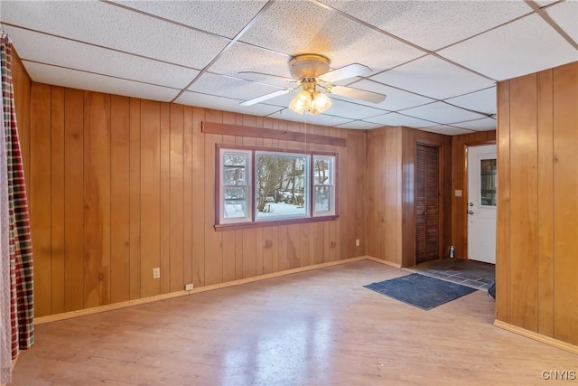 spare room featuring a drop ceiling, wood-type flooring, wooden walls, and ceiling fan