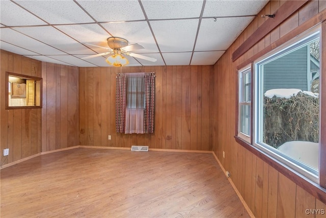 unfurnished room featuring wood-type flooring, ceiling fan, a drop ceiling, and wooden walls