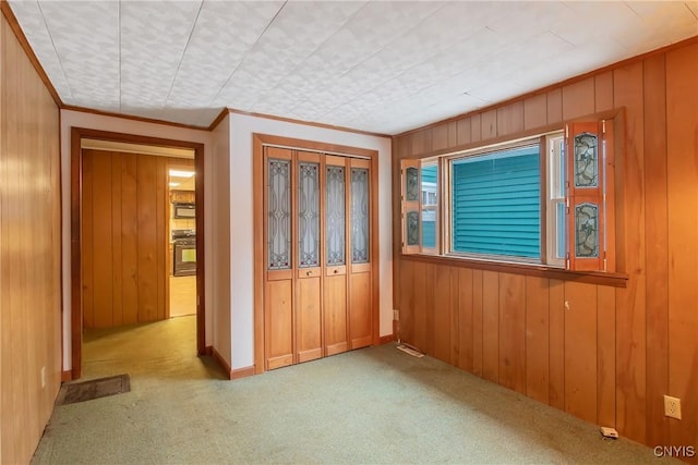 carpeted empty room with crown molding and wood walls