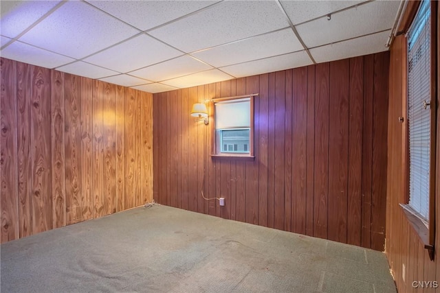 carpeted spare room featuring a drop ceiling and wood walls