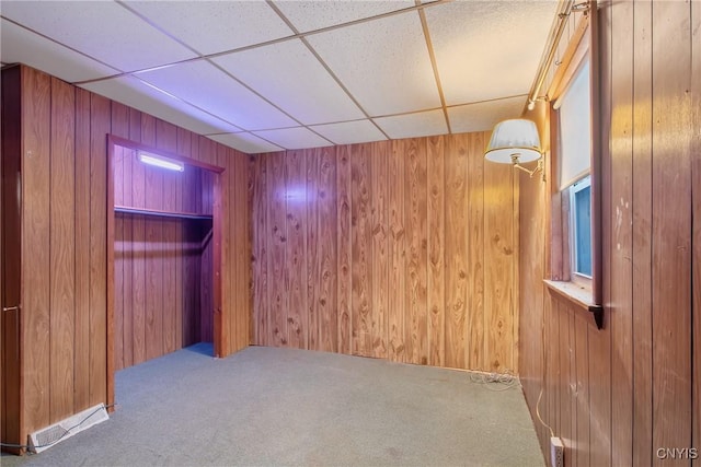 basement featuring a drop ceiling, carpet, and wood walls