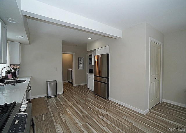 kitchen featuring white cabinetry, wood-type flooring, sink, and stainless steel refrigerator