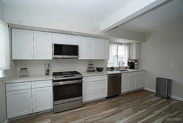 kitchen featuring stainless steel appliances, white cabinetry, sink, and beam ceiling