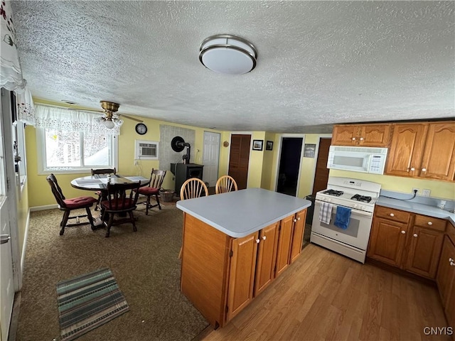 kitchen featuring a textured ceiling, an AC wall unit, light hardwood / wood-style flooring, a kitchen island, and white appliances