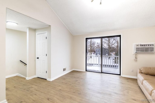 unfurnished living room with a wall unit AC, light hardwood / wood-style floors, and vaulted ceiling