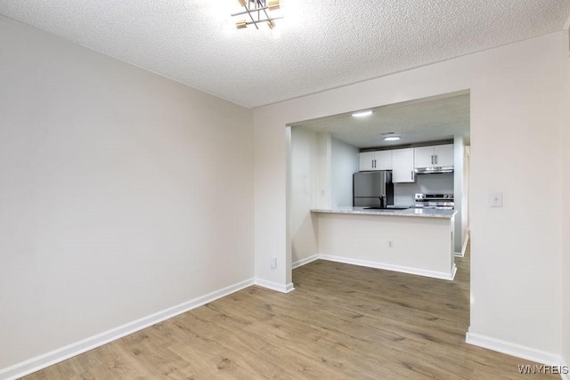 kitchen featuring a textured ceiling, appliances with stainless steel finishes, kitchen peninsula, hardwood / wood-style floors, and white cabinets