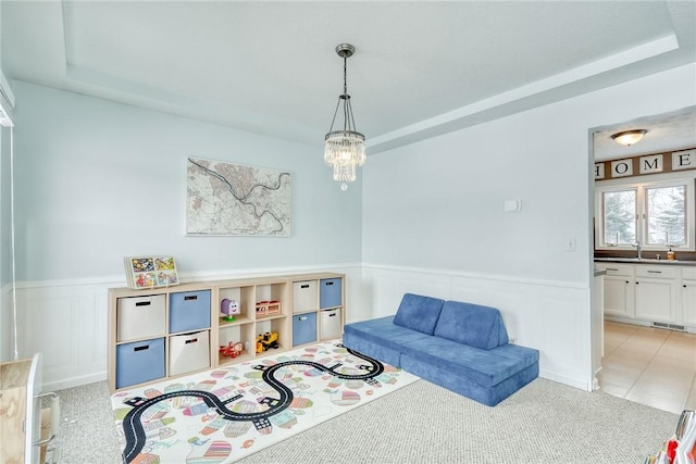 playroom with light colored carpet, a tray ceiling, a chandelier, and sink