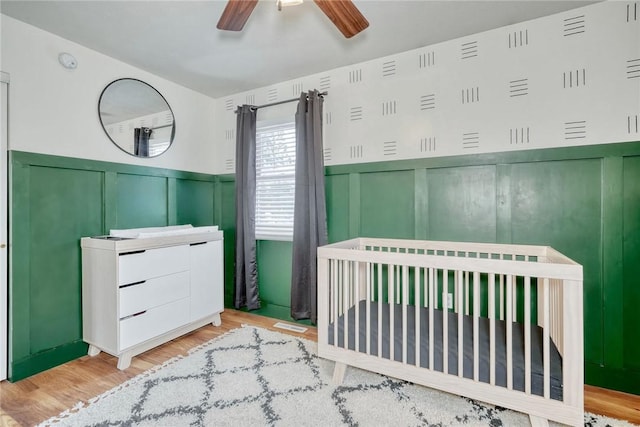 bedroom featuring a nursery area, ceiling fan, and light wood-type flooring