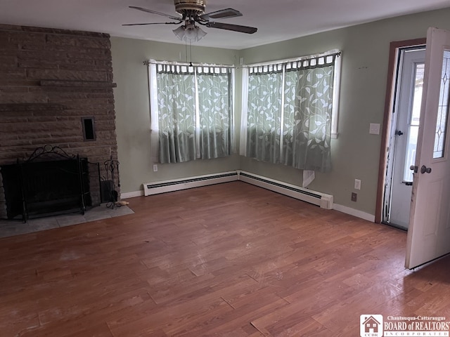 unfurnished living room with a stone fireplace, wood-type flooring, a baseboard radiator, and ceiling fan