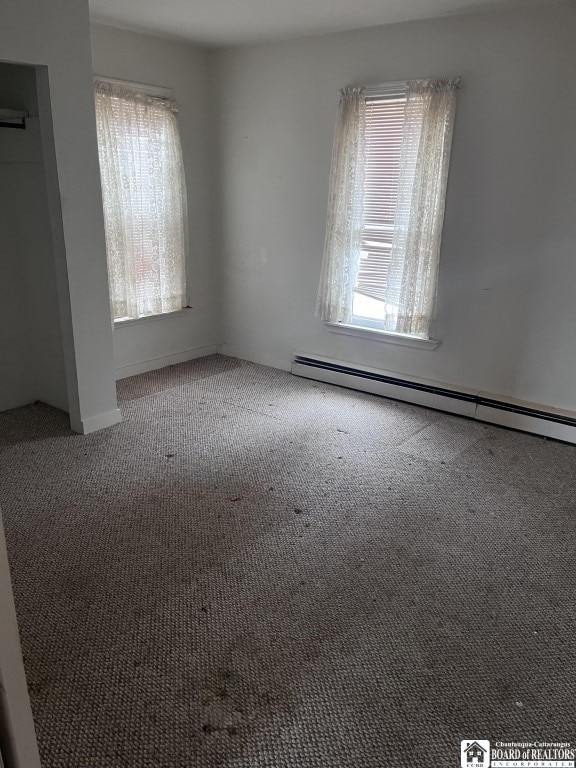 carpeted empty room featuring a baseboard heating unit