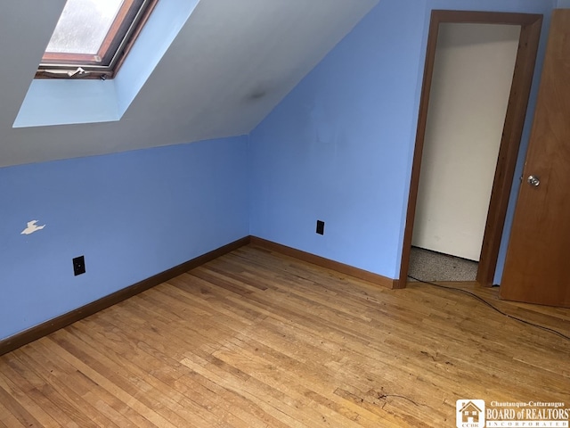 additional living space with vaulted ceiling with skylight and light hardwood / wood-style flooring