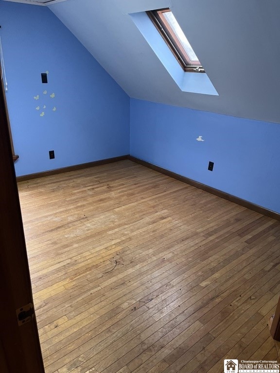 additional living space with light hardwood / wood-style flooring and lofted ceiling with skylight