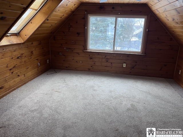 additional living space with wooden walls, vaulted ceiling with skylight, and carpet