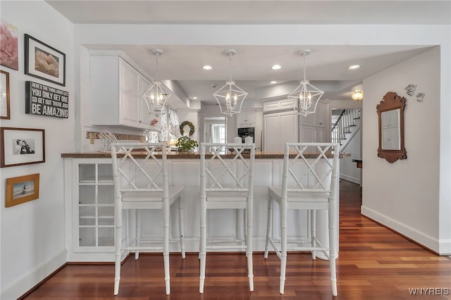 kitchen featuring a breakfast bar, decorative light fixtures, white cabinetry, hardwood / wood-style flooring, and kitchen peninsula