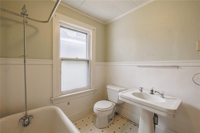 bathroom featuring a bathing tub, ornamental molding, a wealth of natural light, and toilet