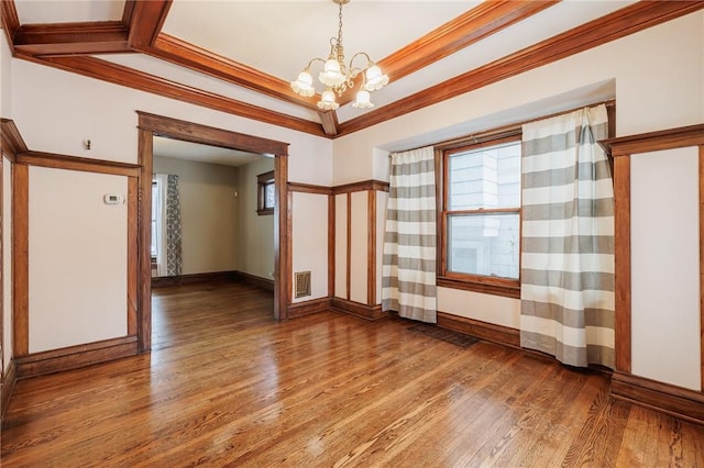 empty room featuring hardwood / wood-style flooring, a healthy amount of sunlight, ornamental molding, and an inviting chandelier