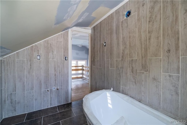 bathroom featuring lofted ceiling, a bath, tile patterned flooring, and tile walls