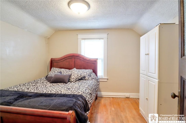 bedroom with vaulted ceiling, a textured ceiling, and light wood-type flooring