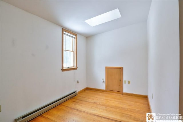 empty room with light wood-type flooring, a skylight, and baseboard heating