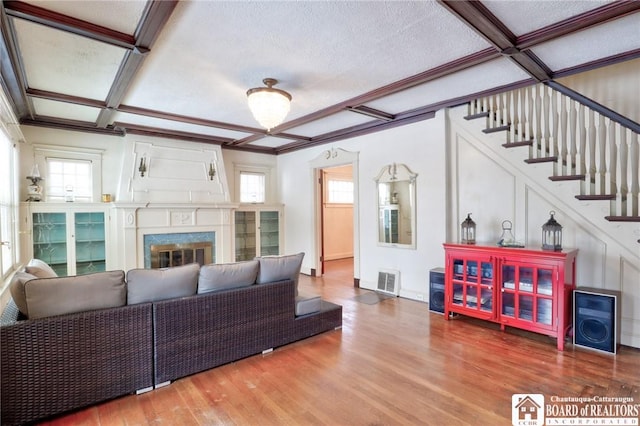 living room with ornamental molding, a premium fireplace, coffered ceiling, and hardwood / wood-style floors