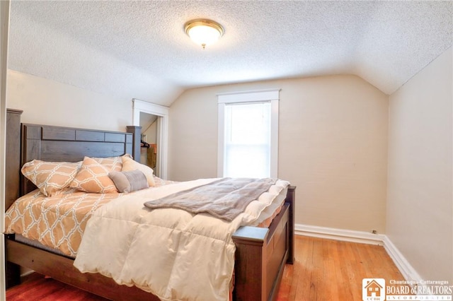 bedroom with light hardwood / wood-style flooring, a textured ceiling, and vaulted ceiling