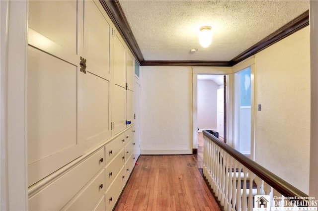 corridor with crown molding, a textured ceiling, and light wood-type flooring