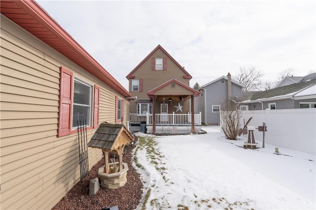 snow covered back of property featuring covered porch