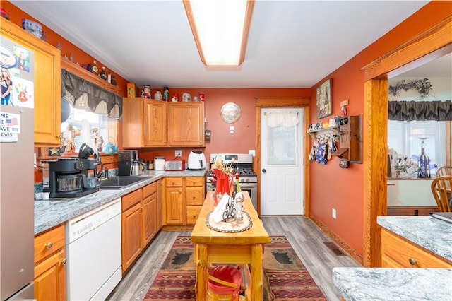 kitchen featuring light wood-type flooring, stainless steel range with gas stovetop, white dishwasher, a healthy amount of sunlight, and light stone countertops