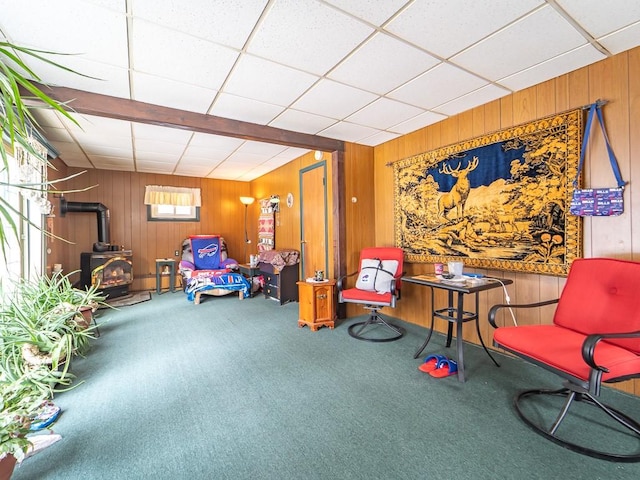 sitting room featuring a wood stove, a paneled ceiling, wood walls, and carpet flooring