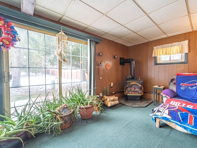 living area with carpet, a wood stove, a drop ceiling, and wood walls