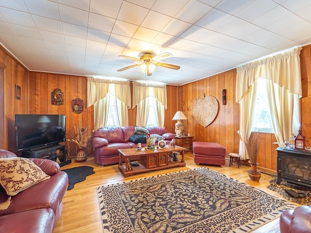 living room with plenty of natural light, a wood stove, ceiling fan, and light wood-type flooring