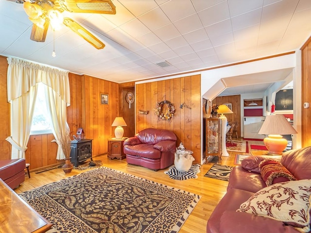 living room with wood-type flooring, wooden walls, ceiling fan, and a wood stove