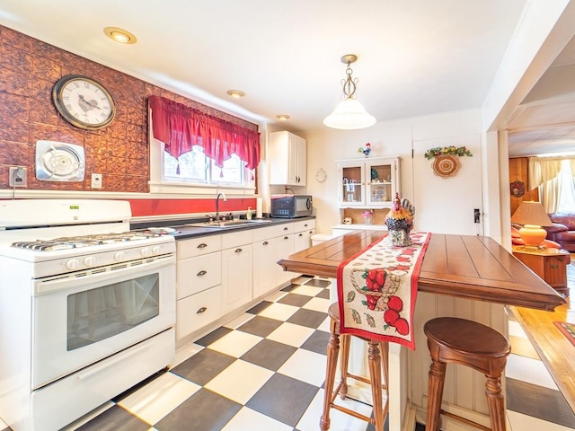 kitchen featuring a healthy amount of sunlight, sink, white gas range oven, and white cabinets