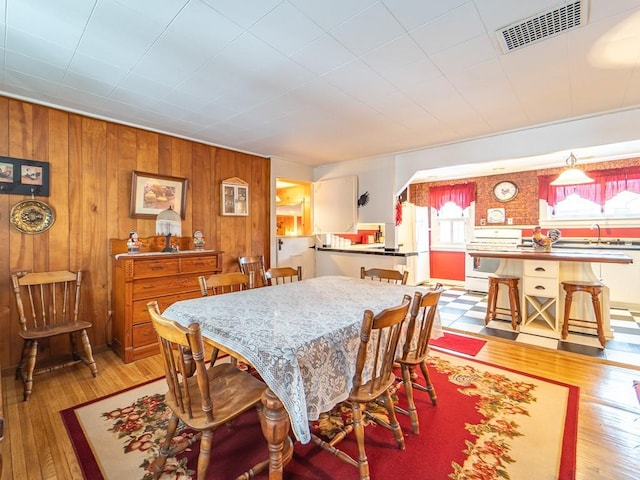 dining room with sink, light hardwood / wood-style flooring, and wood walls