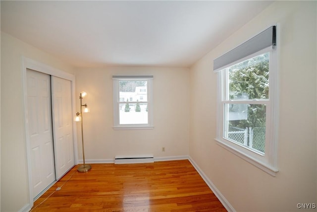 unfurnished bedroom featuring a closet, baseboard heating, and light hardwood / wood-style flooring