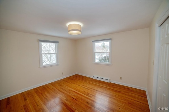 empty room with hardwood / wood-style floors, a healthy amount of sunlight, and baseboard heating