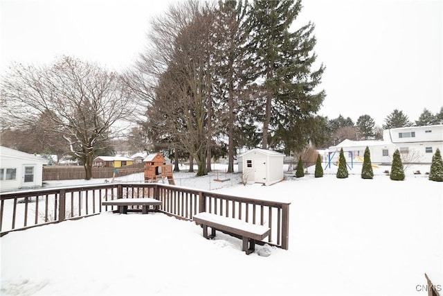 snow covered deck featuring a storage shed and a playground