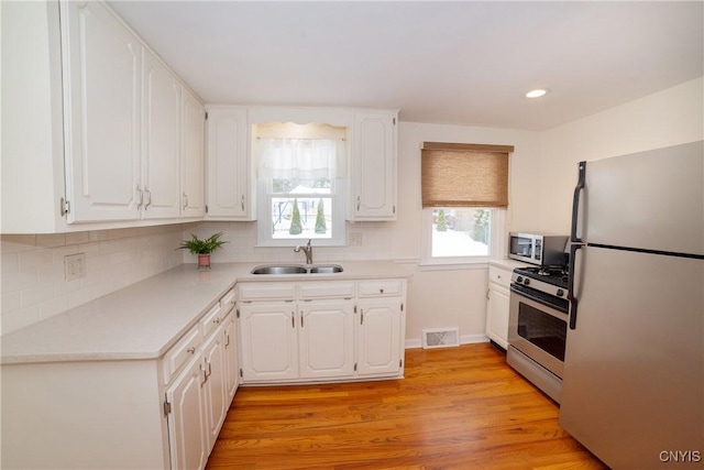 kitchen with sink, backsplash, white cabinets, light hardwood / wood-style floors, and stainless steel appliances