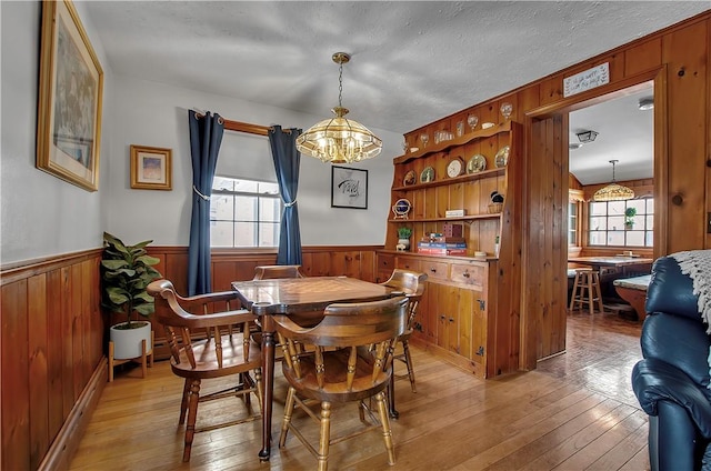 dining space with wood walls, a textured ceiling, and light wood-type flooring