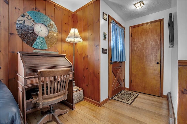 foyer featuring a baseboard radiator, a textured ceiling, light wood-type flooring, and wood walls