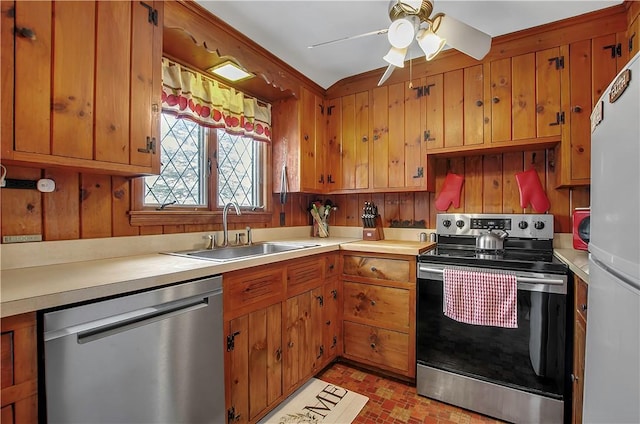 kitchen featuring ceiling fan, appliances with stainless steel finishes, wooden walls, and sink